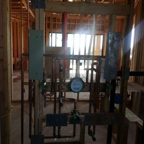 Indoor construction wall framing with exposed pipes, valves, and a central gauge in unfinished room