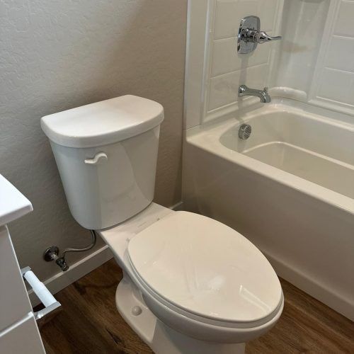 Bathroom with white toilet beside a beige bathtub and wood-look floor.