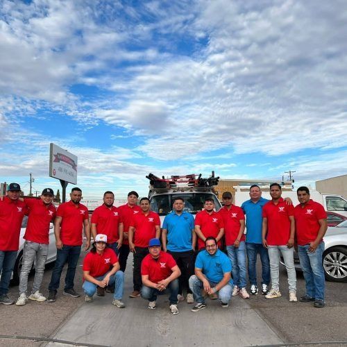 Group of people in red shirts posing outdoors beside a vehicle under a cloudy sky