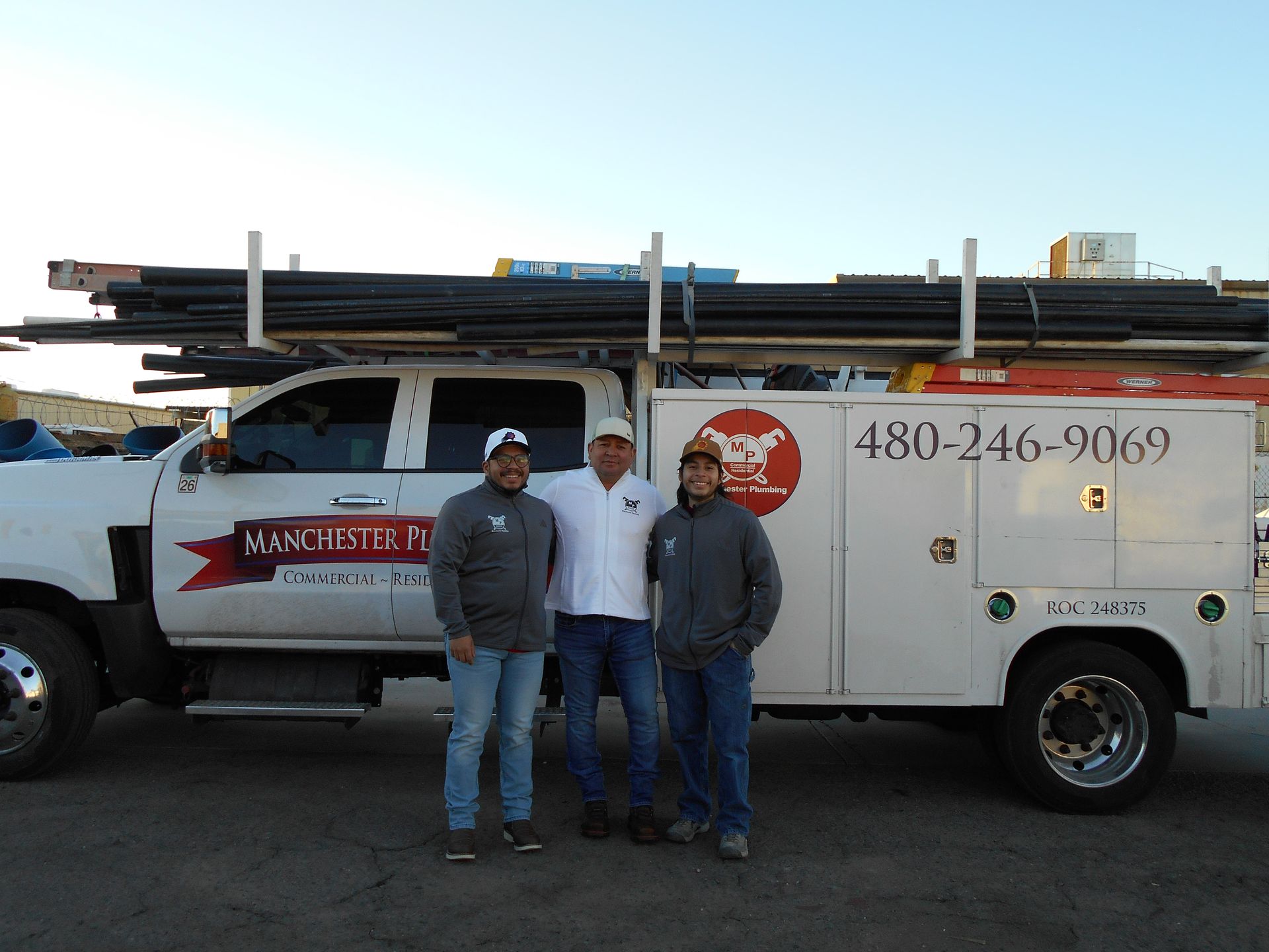 Three men standing in front of a white service truck with ladders on top.