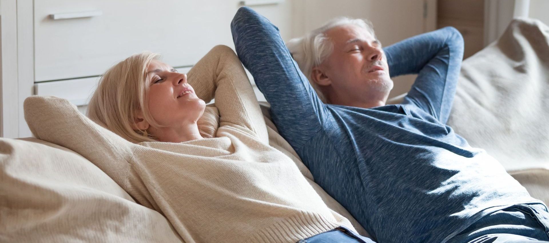 An elderly couple is sitting on a couch looking at a tablet.