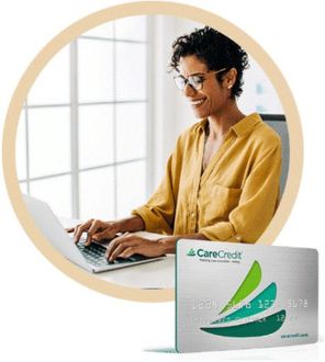 A woman is typing on a laptop next to a carecredit card
