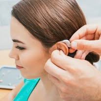 A person is having a hearing aid fitted into their ear by another individual.