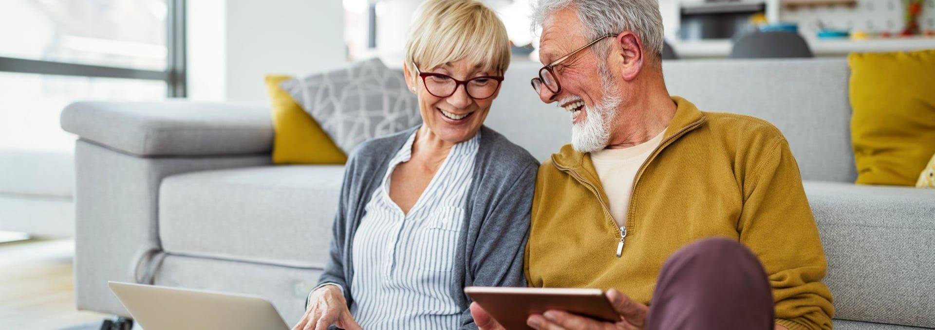 An elderly couple is sitting on a couch looking at a tablet.