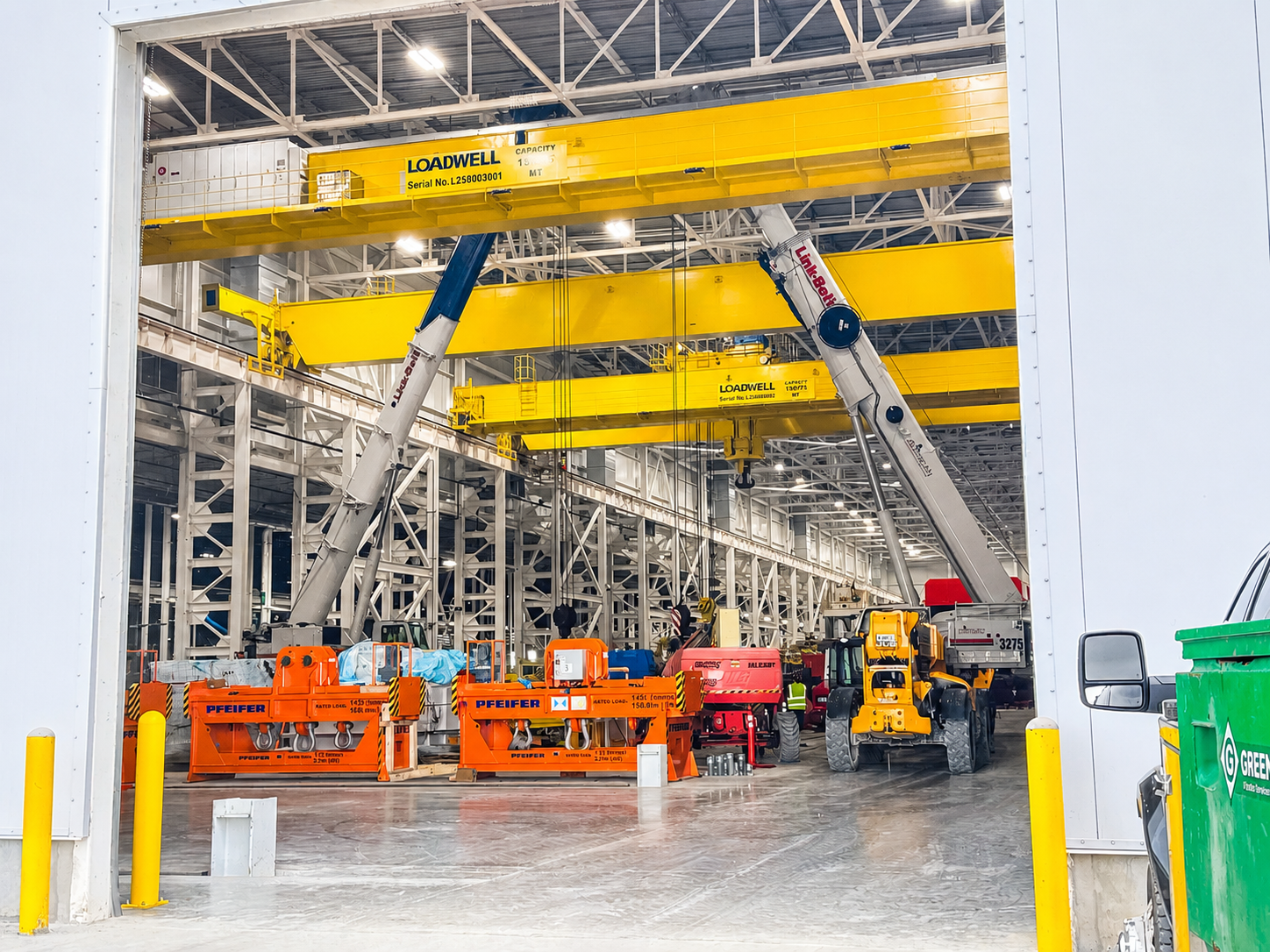 Industrial warehouse with yellow overhead cranes, orange equipment, and a truck loading area