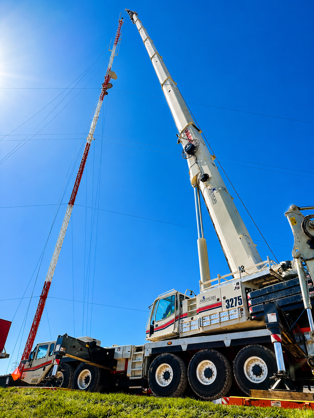 Large crane hoisting a long mast against a clear blue sky at a construction site.