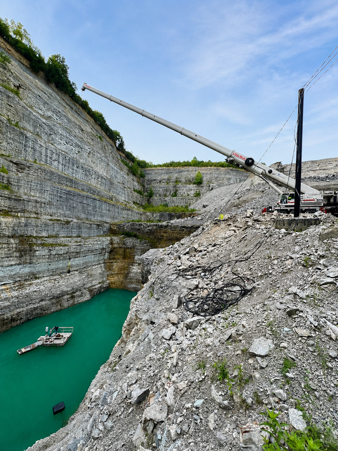 Steep quarry with turquoise water, rocky cliffs, and a crane arm extending over the pit