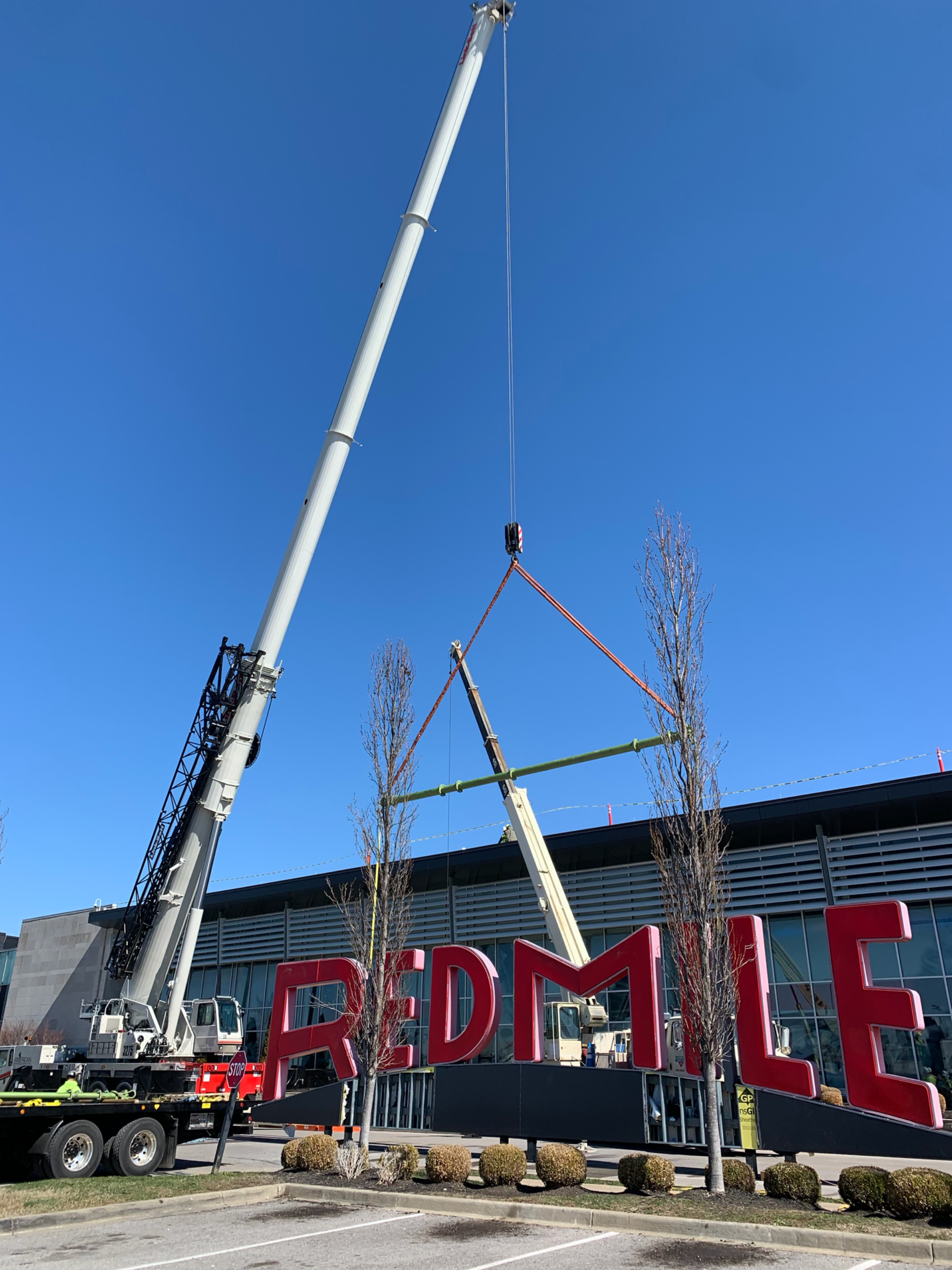 Crane lifting a red “REDMILE” sign into place against a clear blue sky.