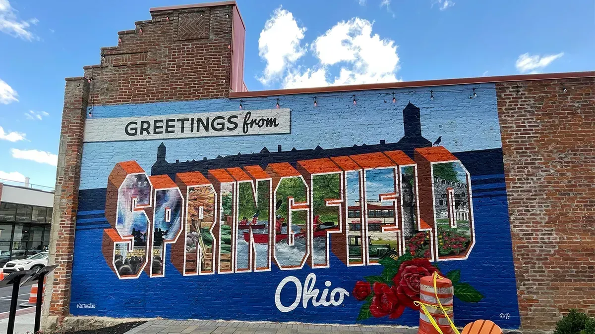 Mural reading “Greetings from Springfield, Ohio” on a brick wall under a blue sky.