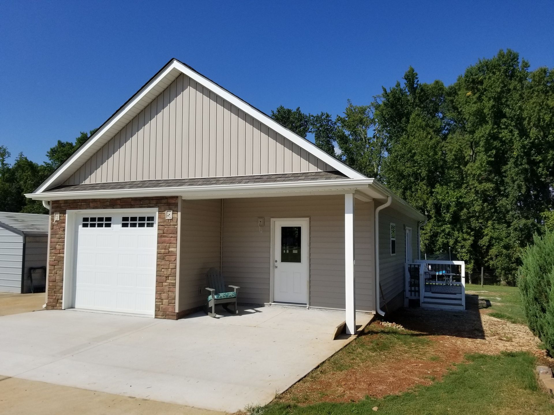 Tan garage with white door and garage door, blue sky, and green trees.
