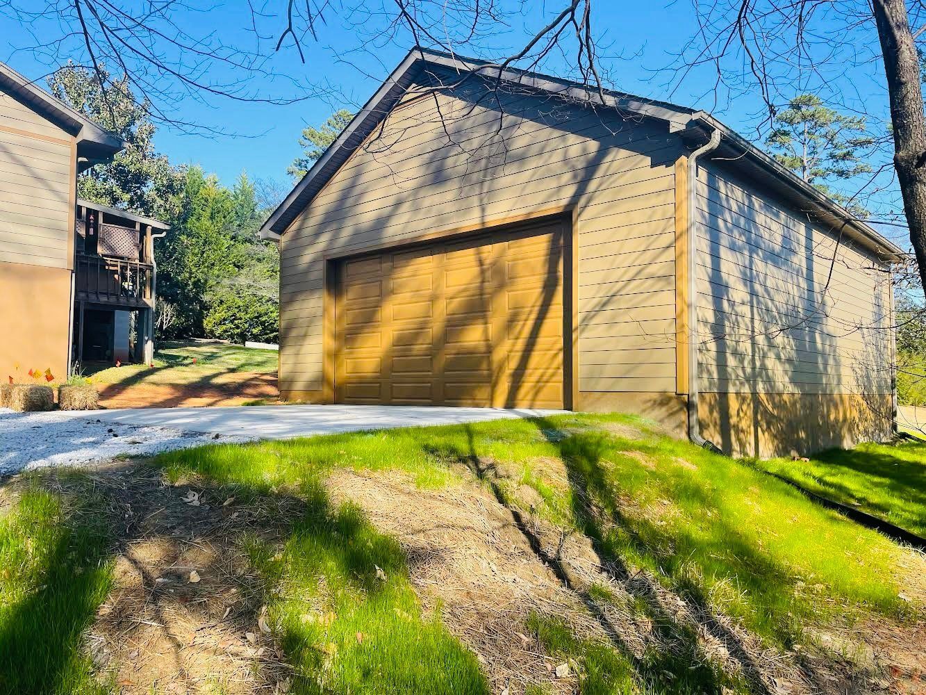 Tan garage with a brown door, in front of a grassy hill.