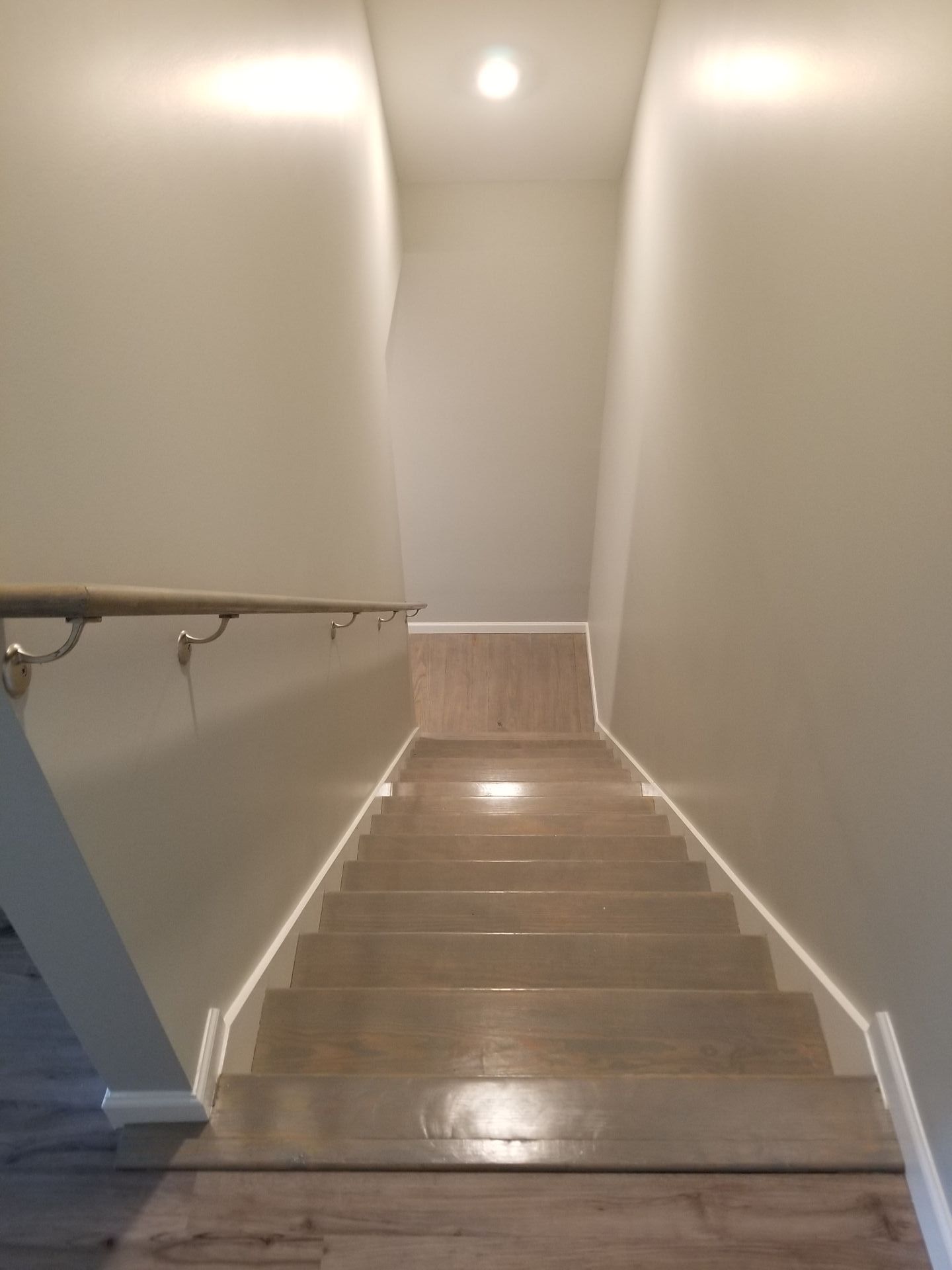 Staircase with light-colored wooden steps, white trim, and a handrail against beige walls.