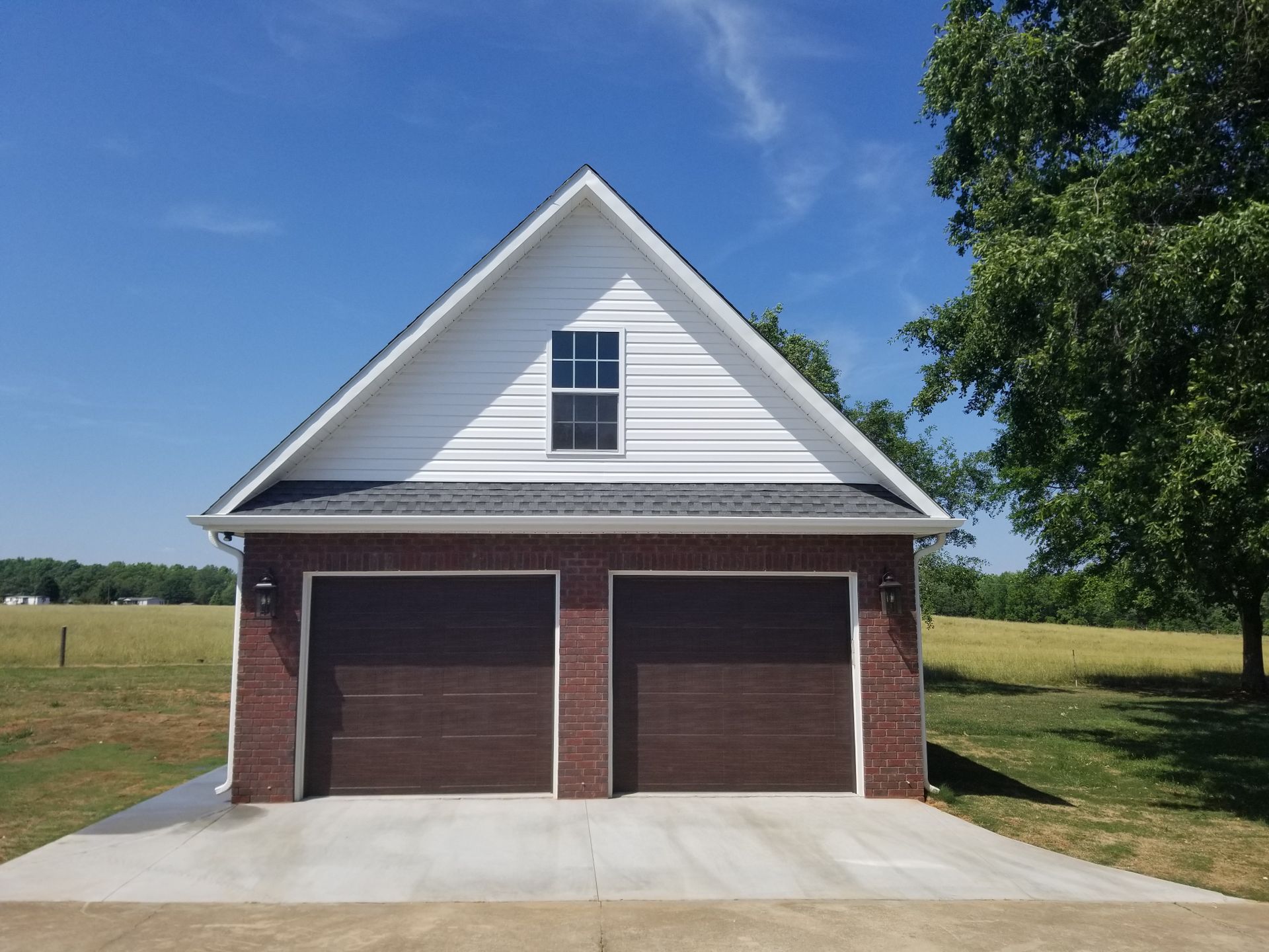 Two-car garage with brown doors and red brick facade under a white gable. Blue sky and rural setting.