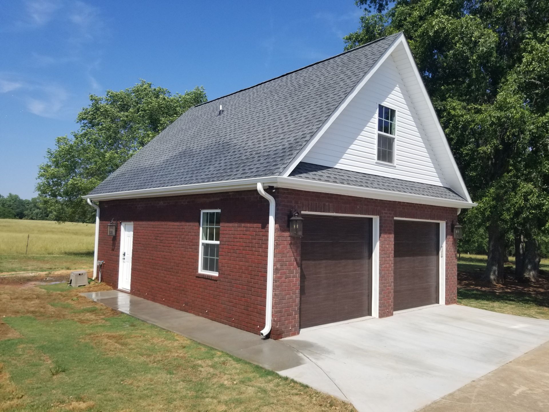 Brick garage with gray roof, white gable, two brown doors, and concrete driveway.