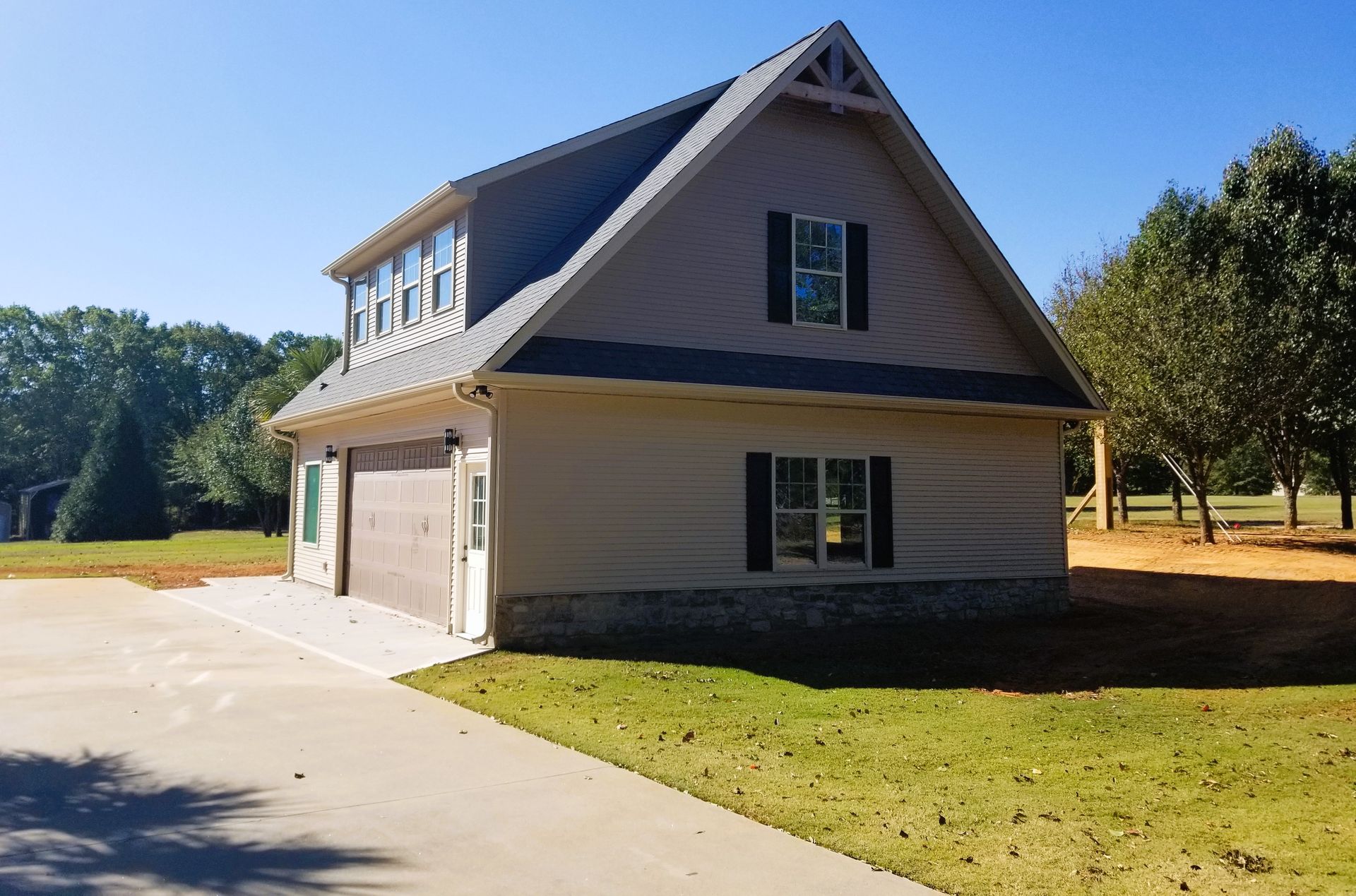 Two-story beige building with garage doors, small windows, and dark shutters; sunny outdoor setting.