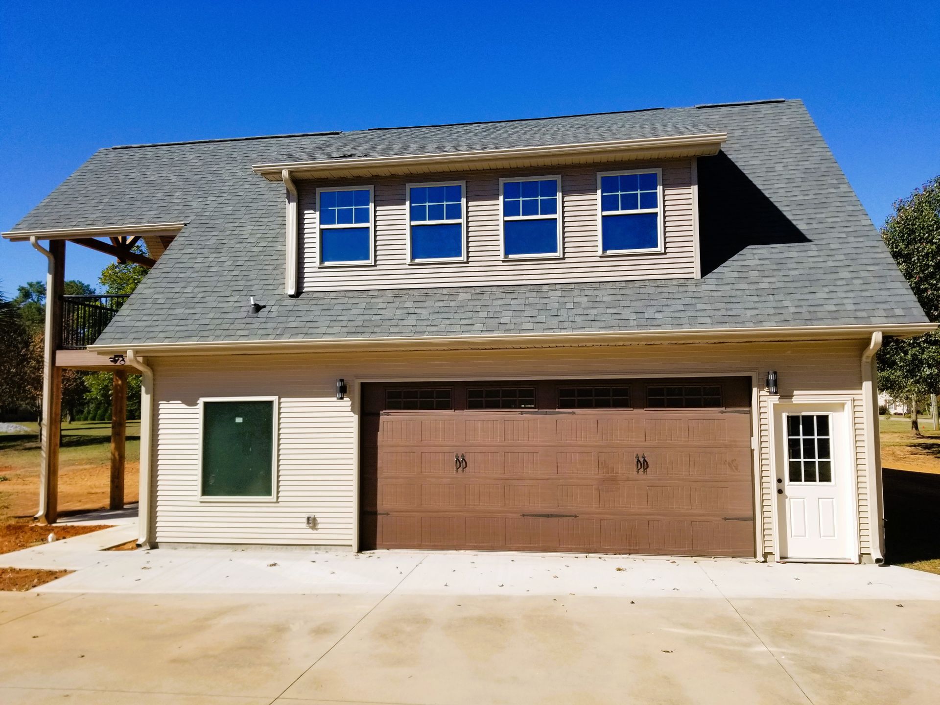 Two-story garage with brown garage door, windows, and light beige siding under a blue sky.