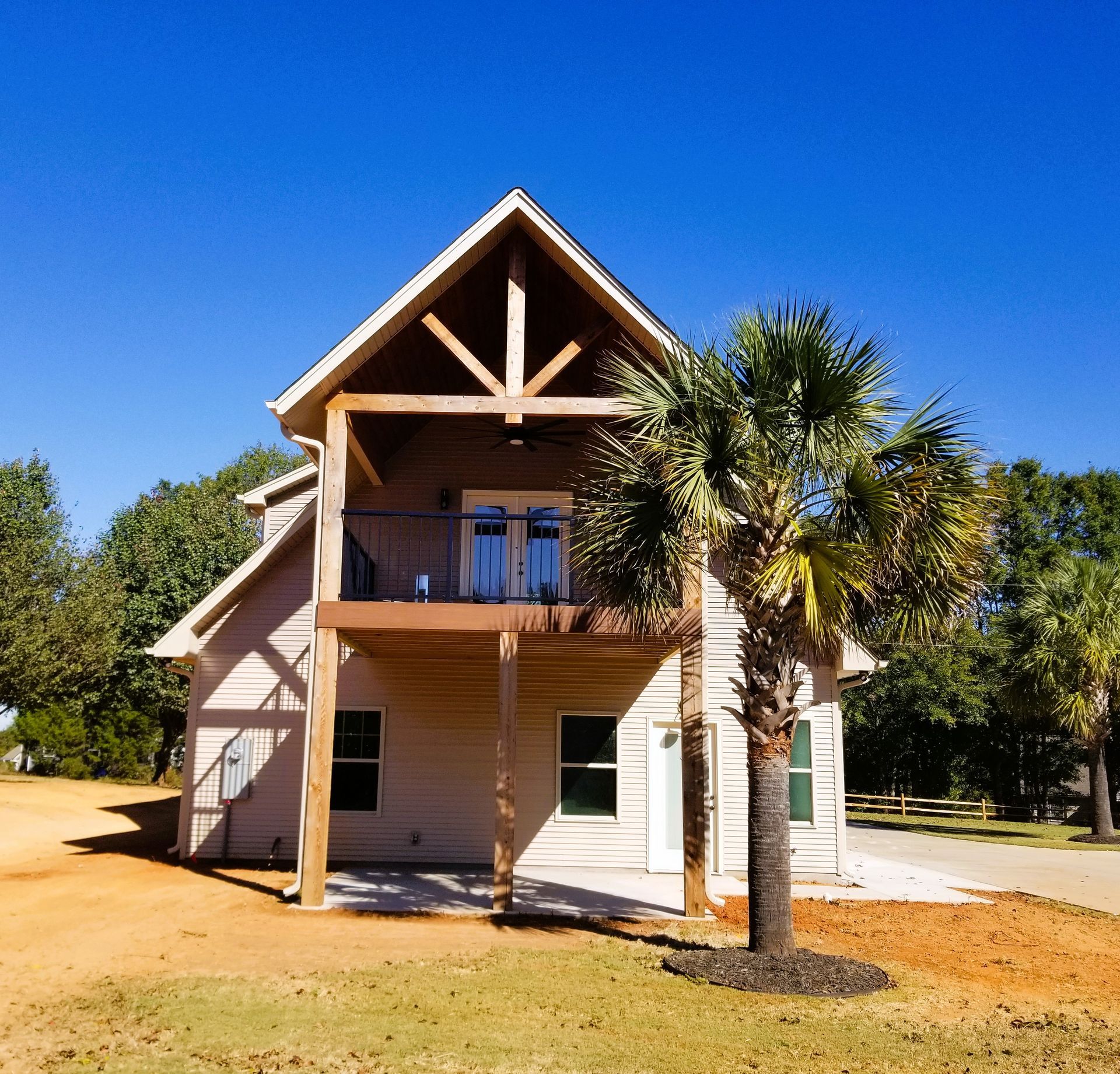 Two-story house with balcony, palm tree, and clear blue sky.