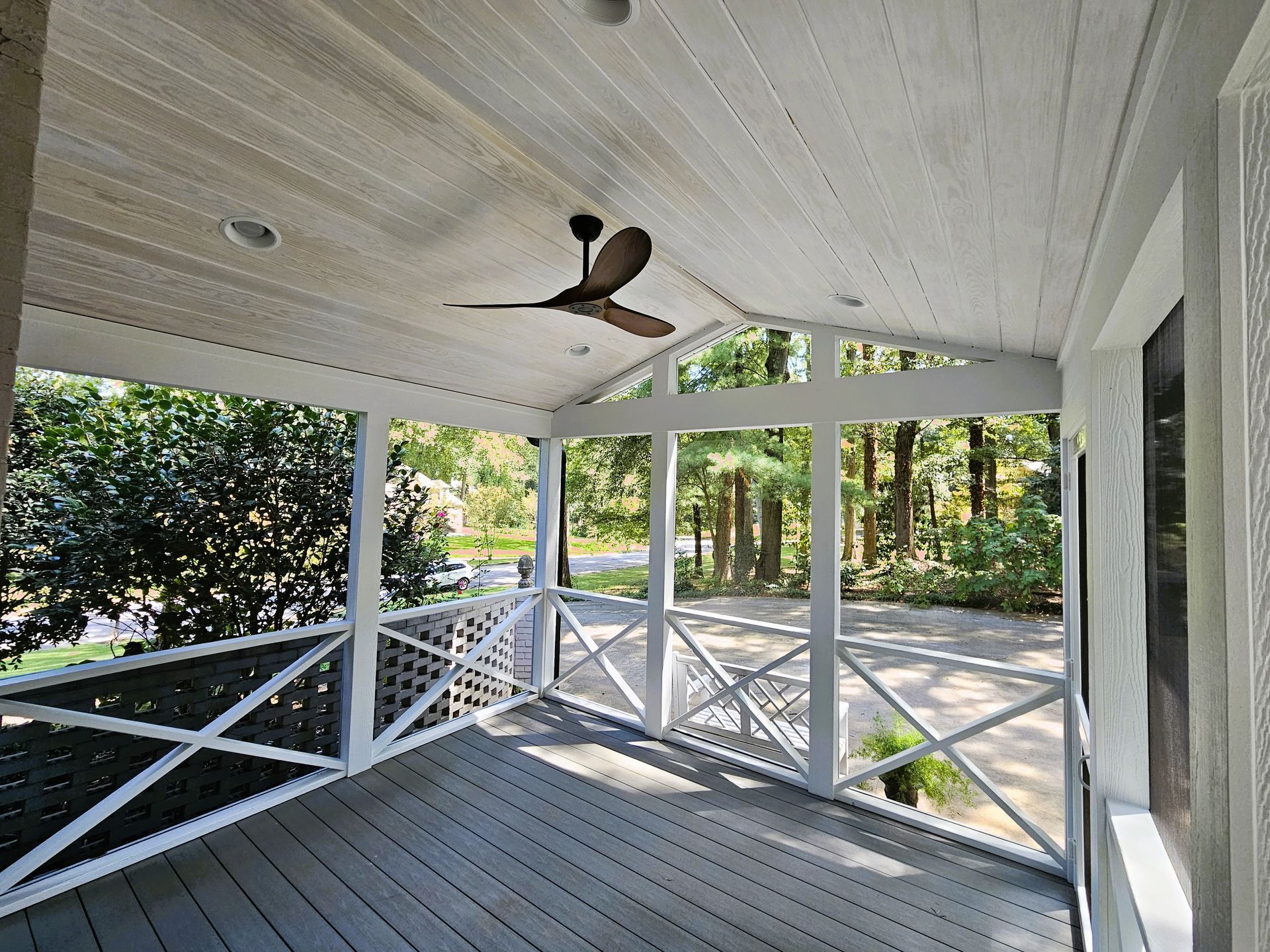 Covered porch with gray floor, white railing and ceiling, ceiling fan, and view of trees.