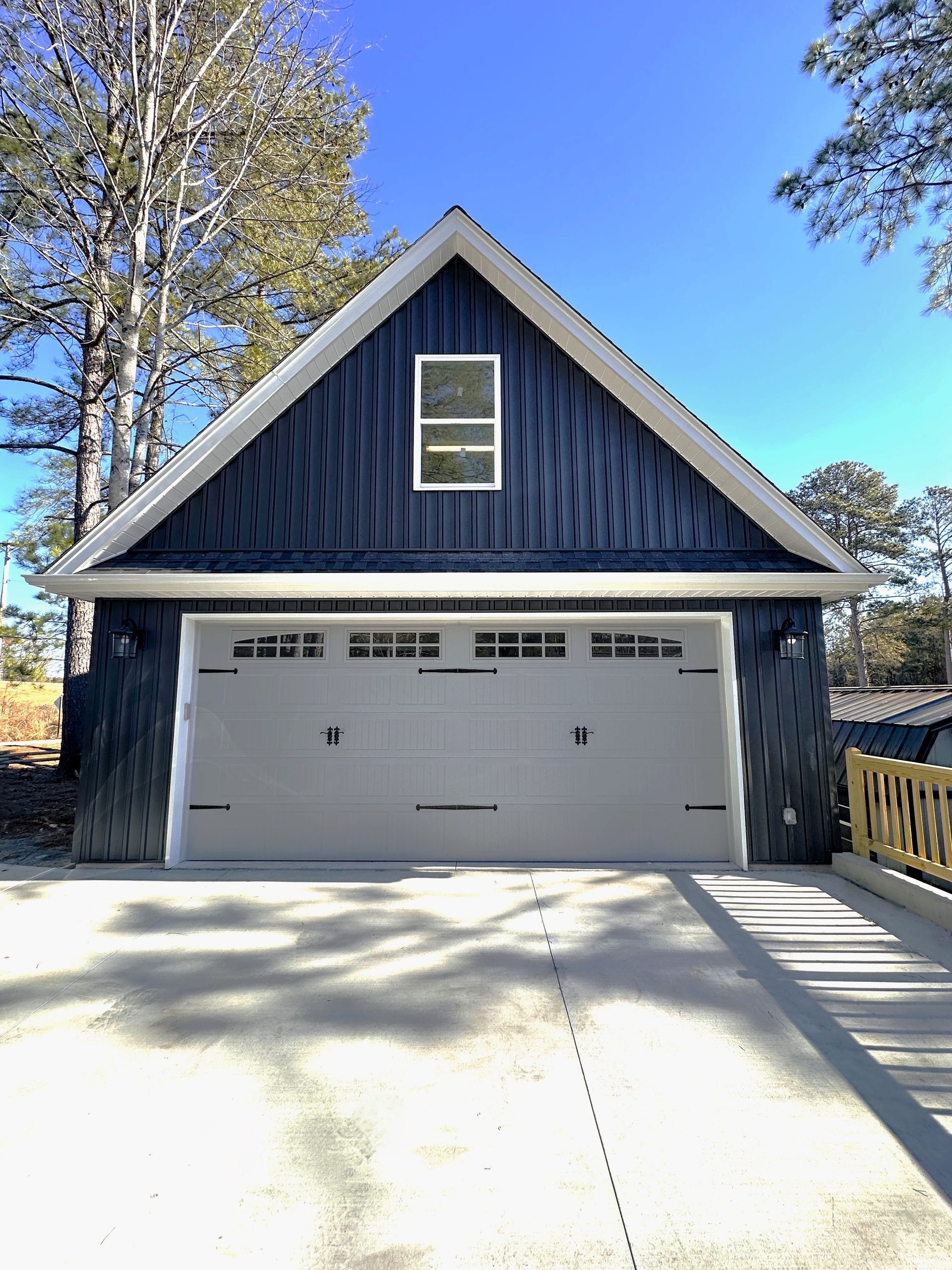 Light gray two-car garage with white doors and trim, concrete driveway, and a small side door.