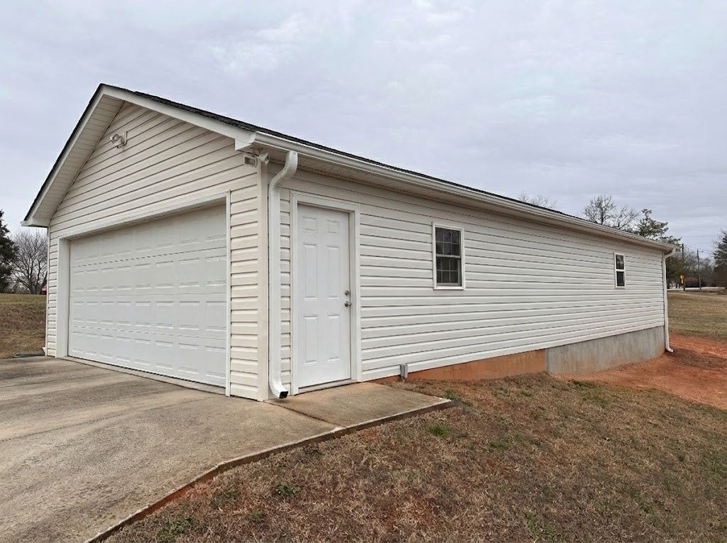 White garage with two-car door, side door, and window. Asphalt driveway leads to the building.