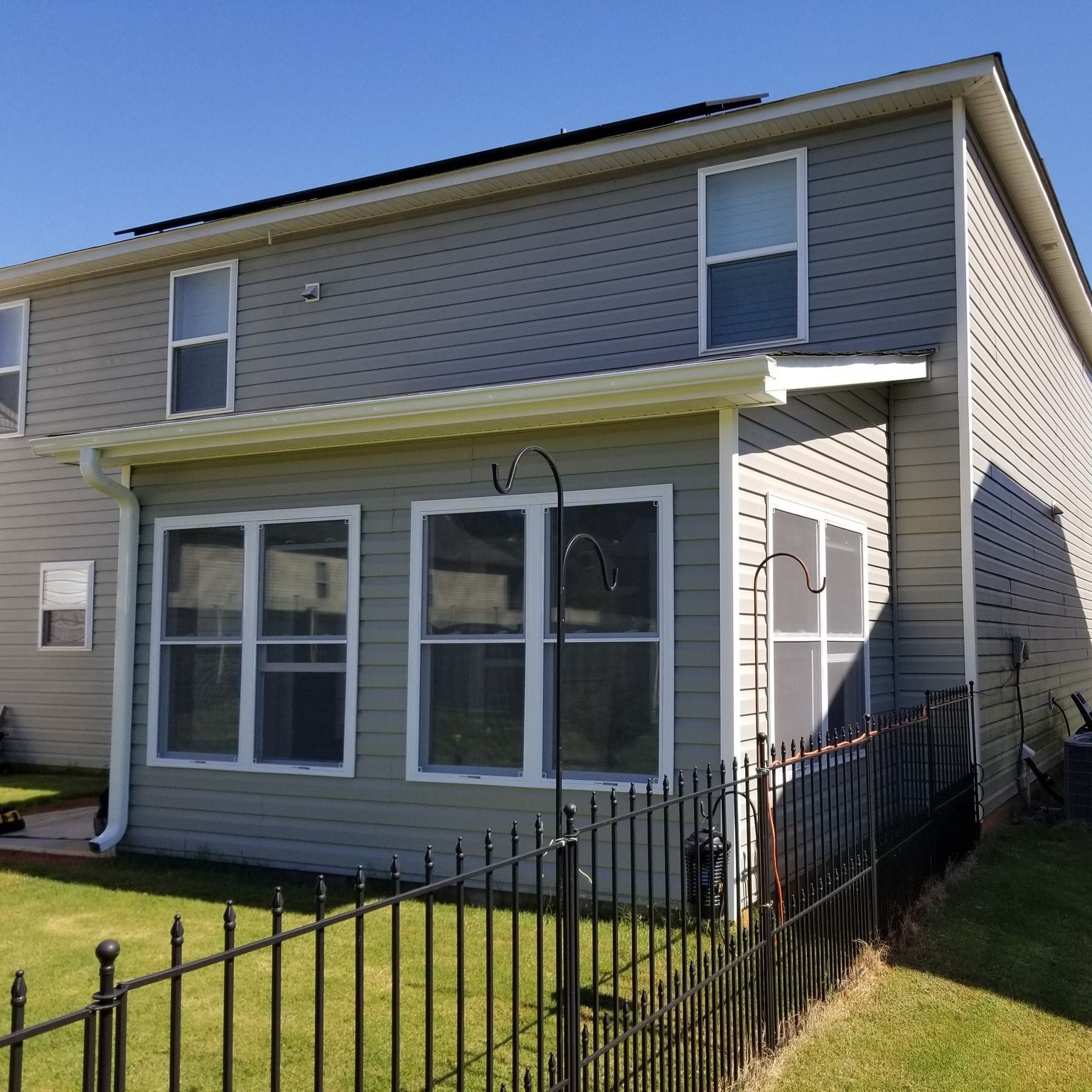 Two-story gray house with a sunroom, black metal fence, and green grass.