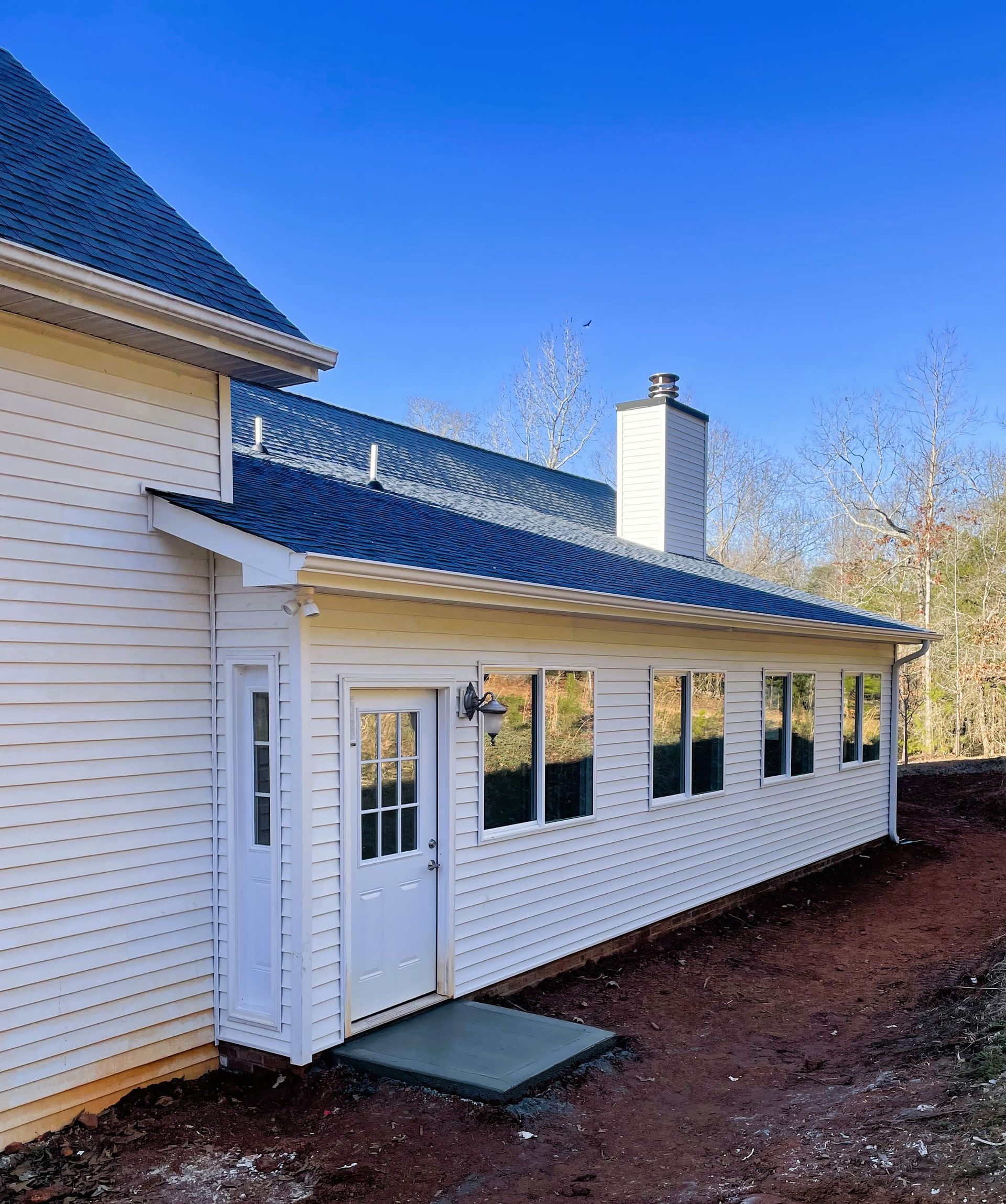 White house with a screened porch and blue roof, nestled on brown soil with a clear blue sky.