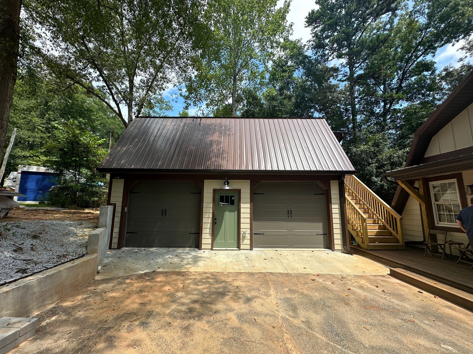 A front view of green garage with wooden steps with window and garage door in view.