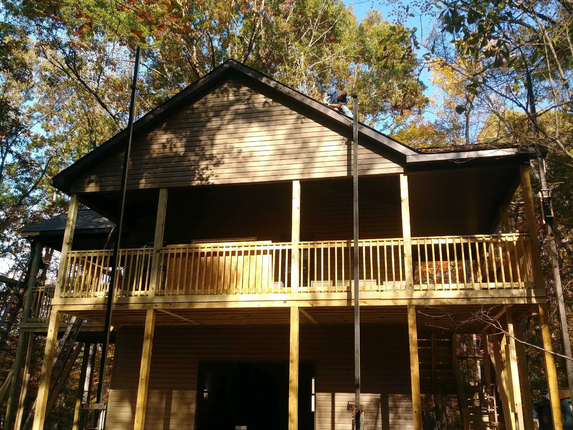 Two-story wooden cabin with a porch under construction, set in a forest of trees.