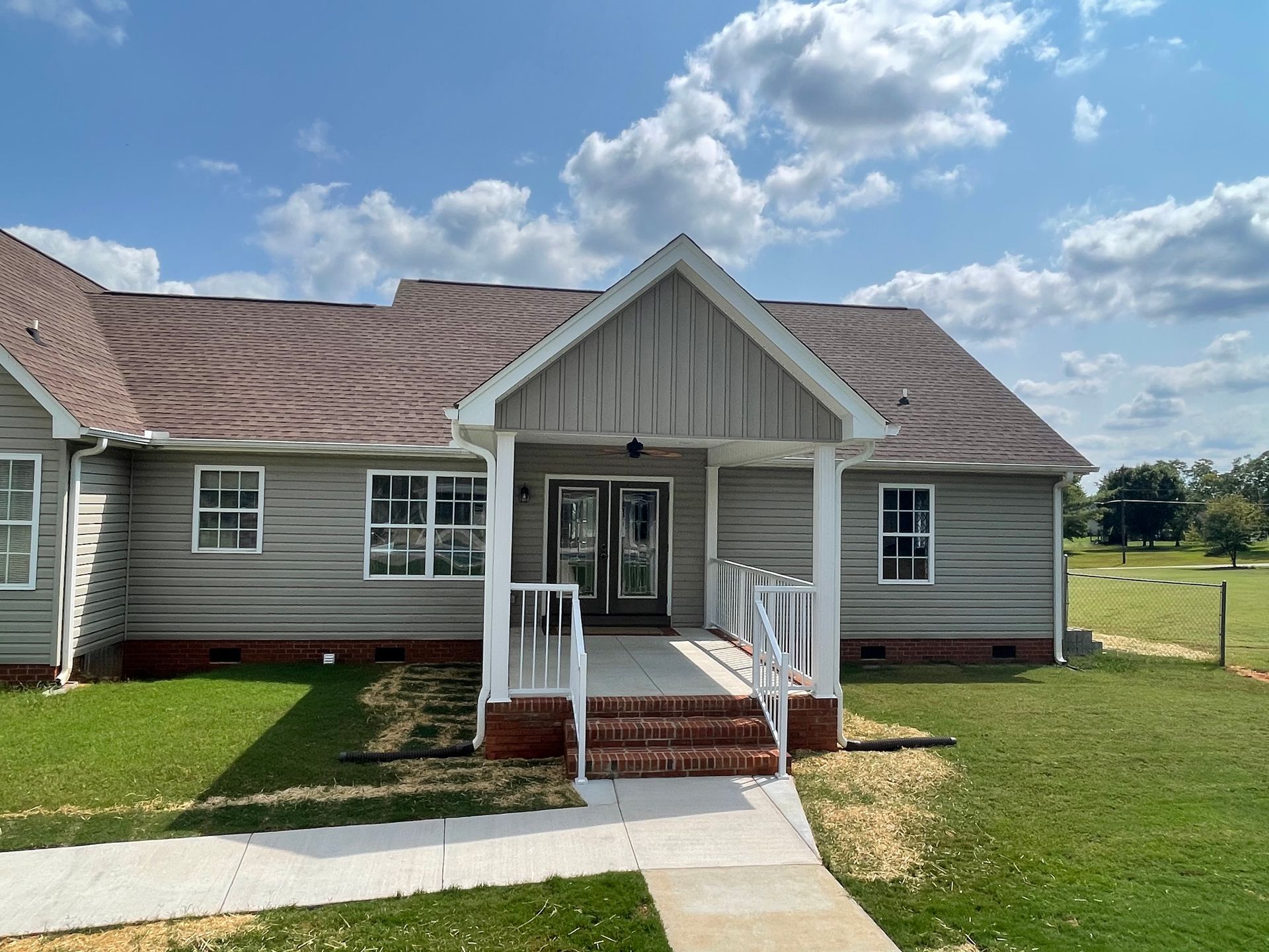 A light gray building with a brown roof and a ramp leading to the front door. Green grass surrounds it.