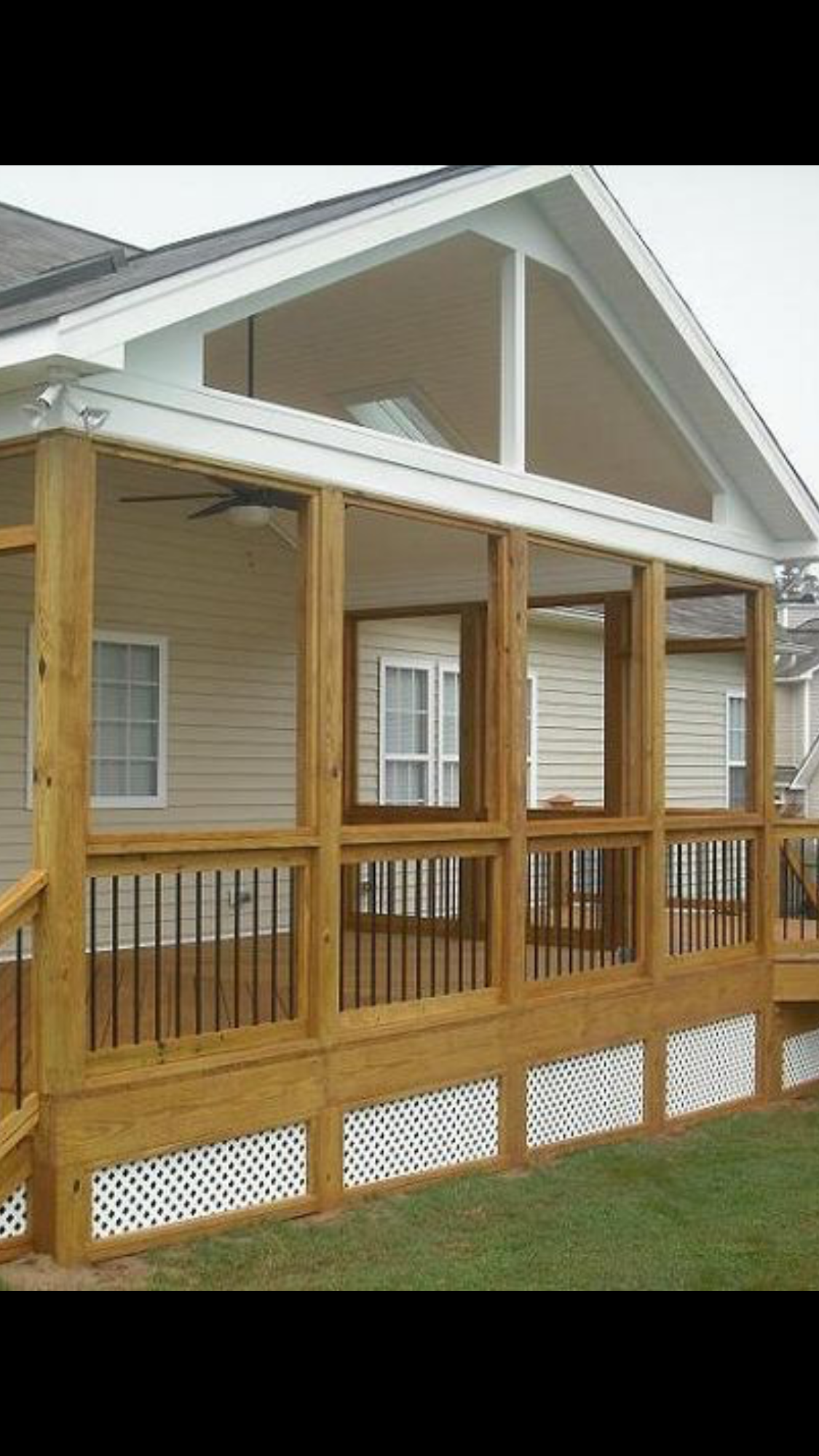Screened porch with wooden deck, columns, and railing, attached to a light-colored house.