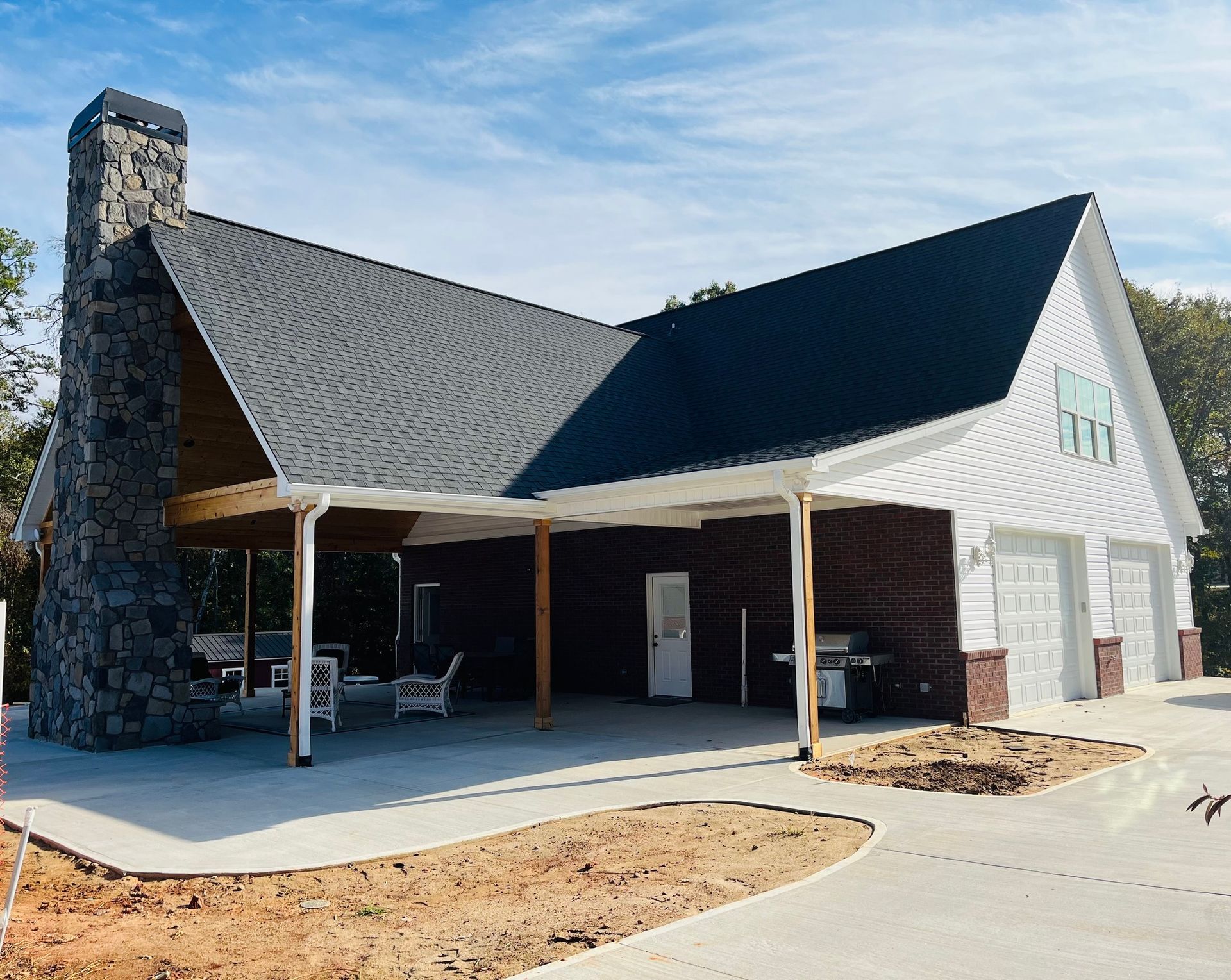 New home with a detached garage, covered patio, and stone chimney; blue sky in the background.