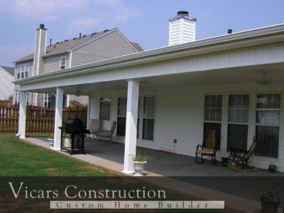 White-columned patio extension on a house with seating, a grill, and grass yard. Vicars Construction logo visible.
