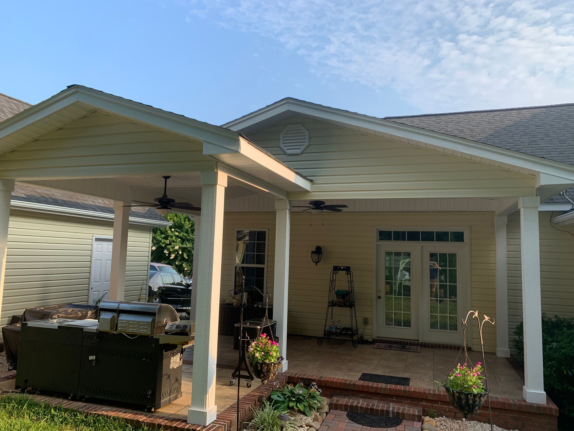 Outdoor patio with a grill under a covered area, a house, and blue sky.