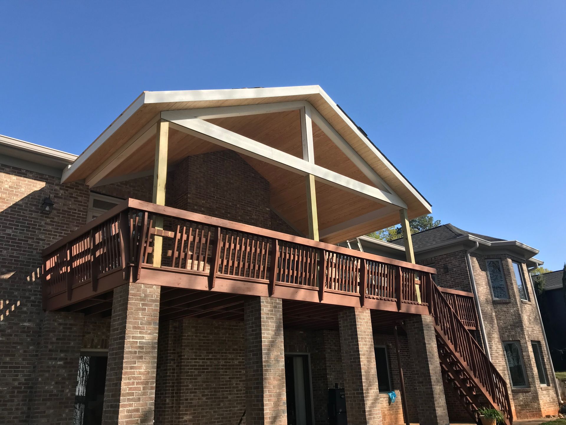 Two-story brick house with wooden deck and gabled roof; blue sky.