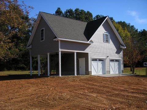 Two-story building with gray siding, a garage, and a dirt yard on a sunny day.