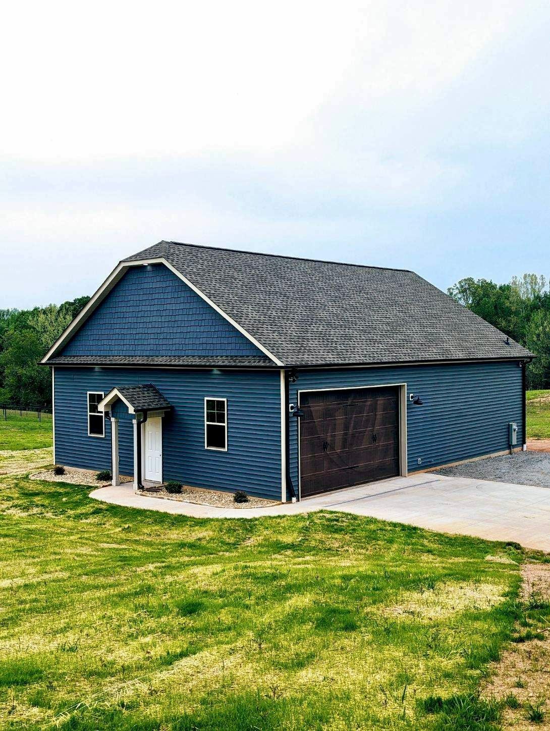 Blue building with a dark garage door, white door, and a gray roof. Set on a green lawn.