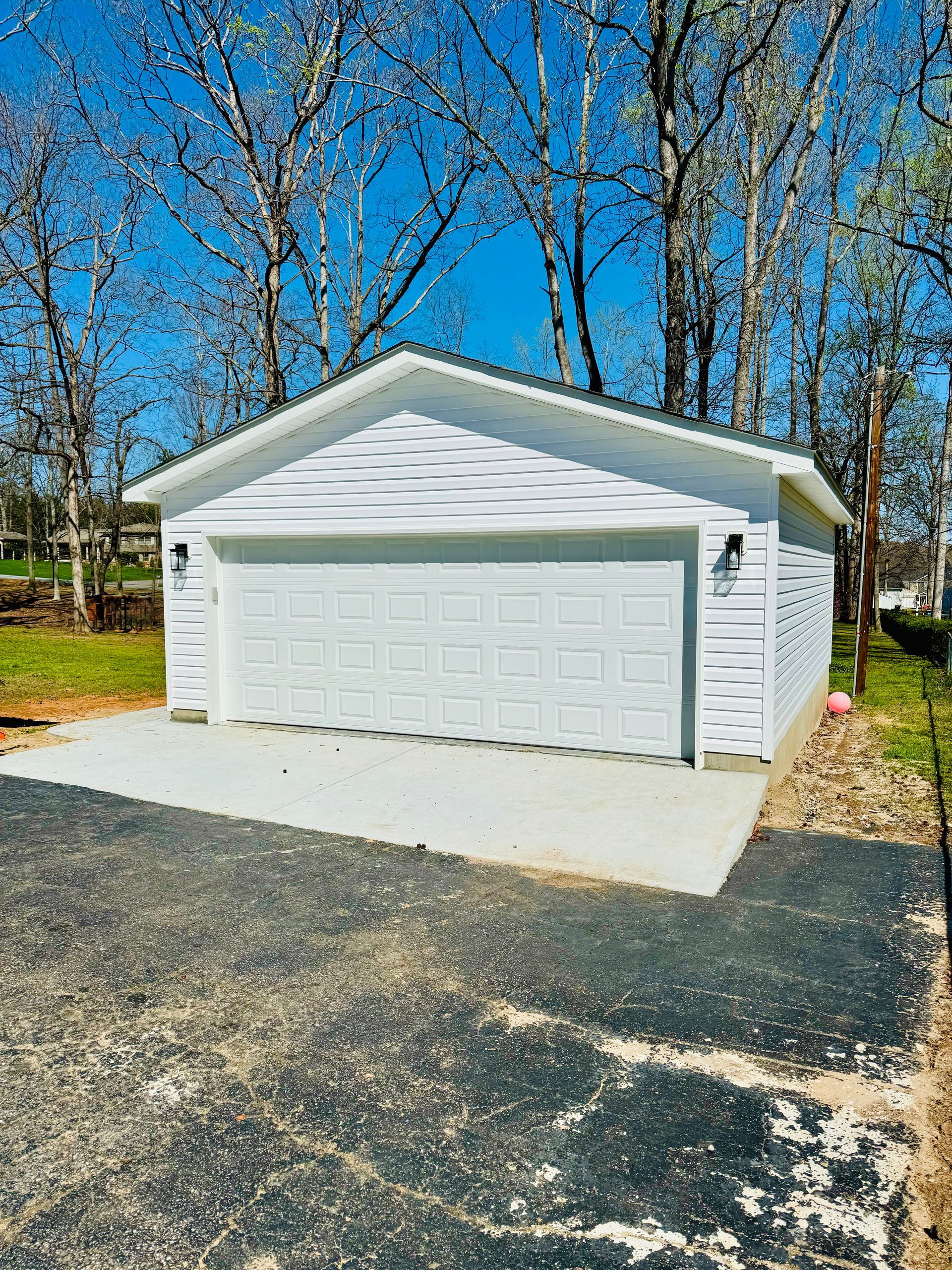A white garage with a concrete driveway and trees in the background.