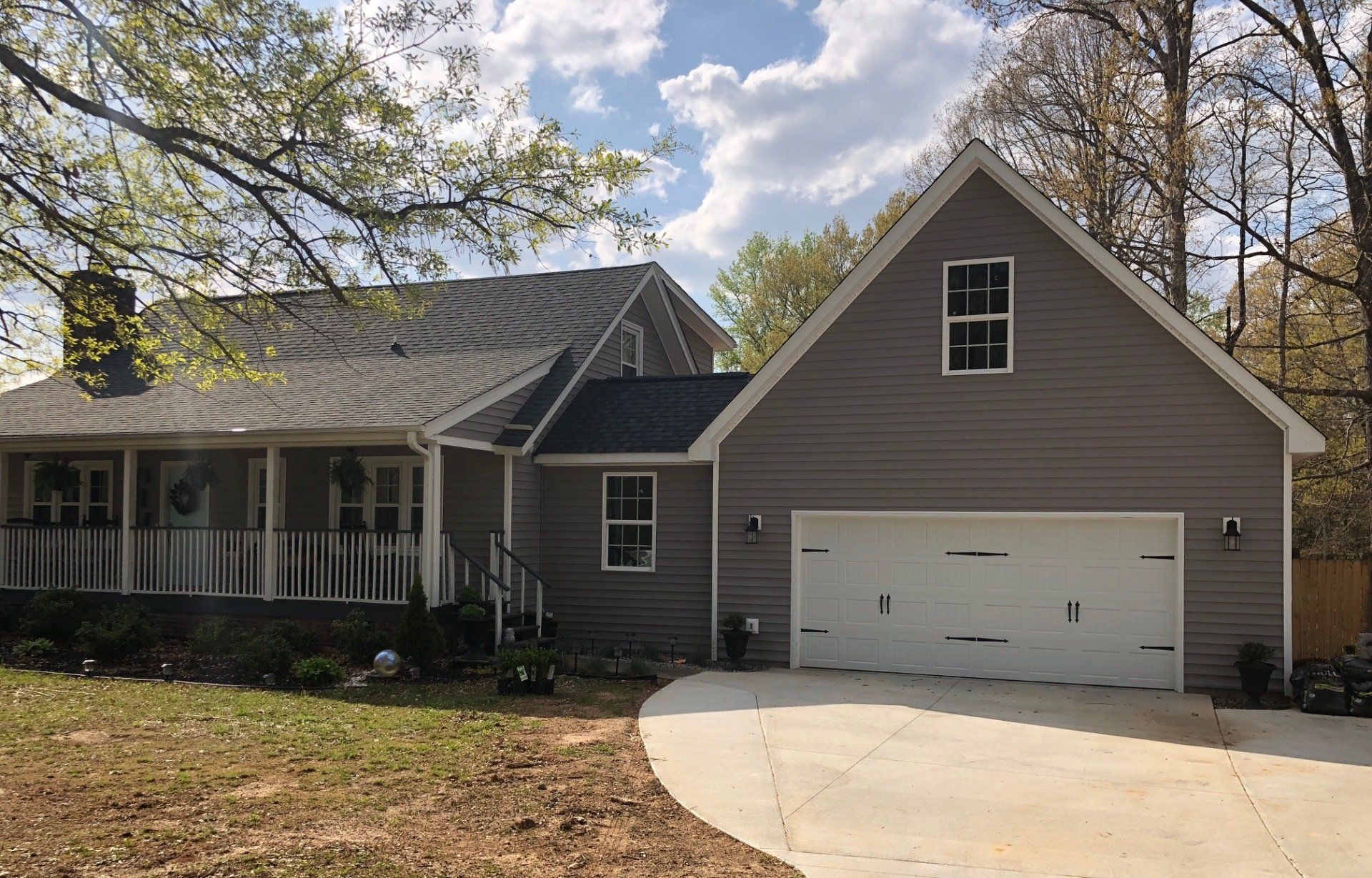 Gray house with white garage door and porch, asphalt driveway, blue sky.