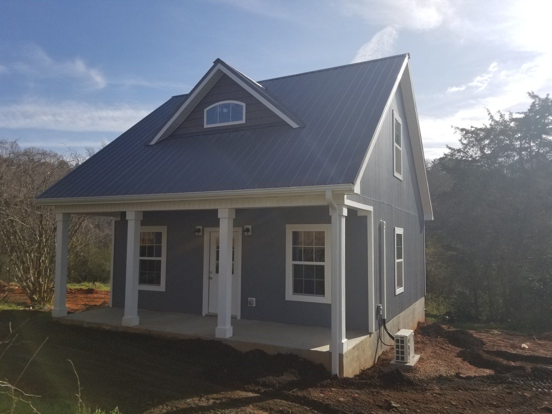 Blue tiny house with porch and metal roof against a sunny sky.