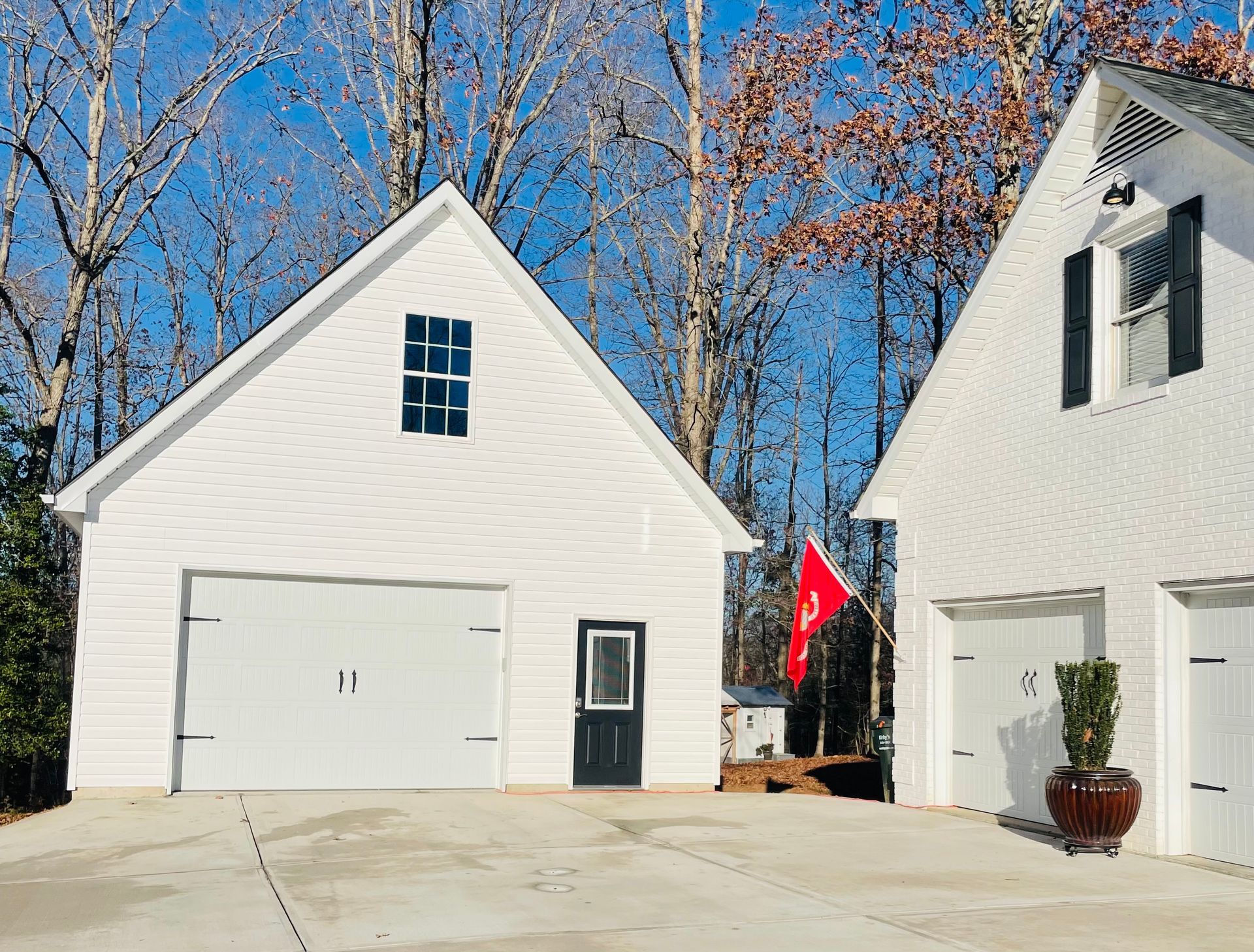 Two white buildings with garage doors, against a backdrop of trees and a blue sky.