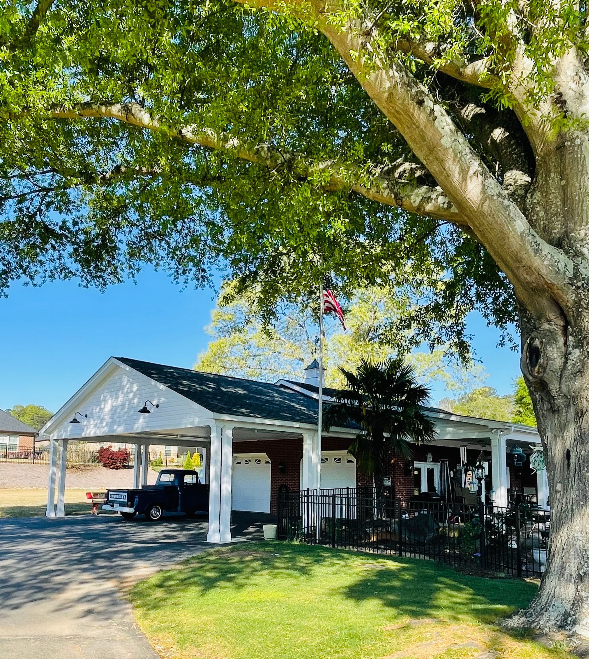 White building with carport, American flag, large tree in sunny outdoor setting.