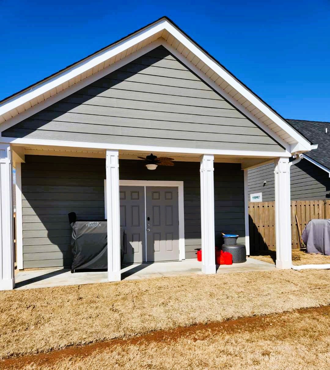 Gray shed with white trim, two doors, and a covered porch on a sunny day.