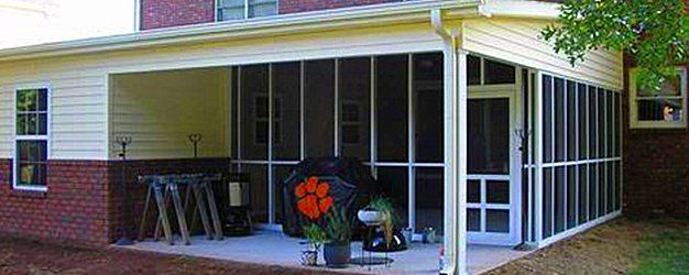 Screened-in porch attached to a brick house. Black grill and Clemson umbrella visible.