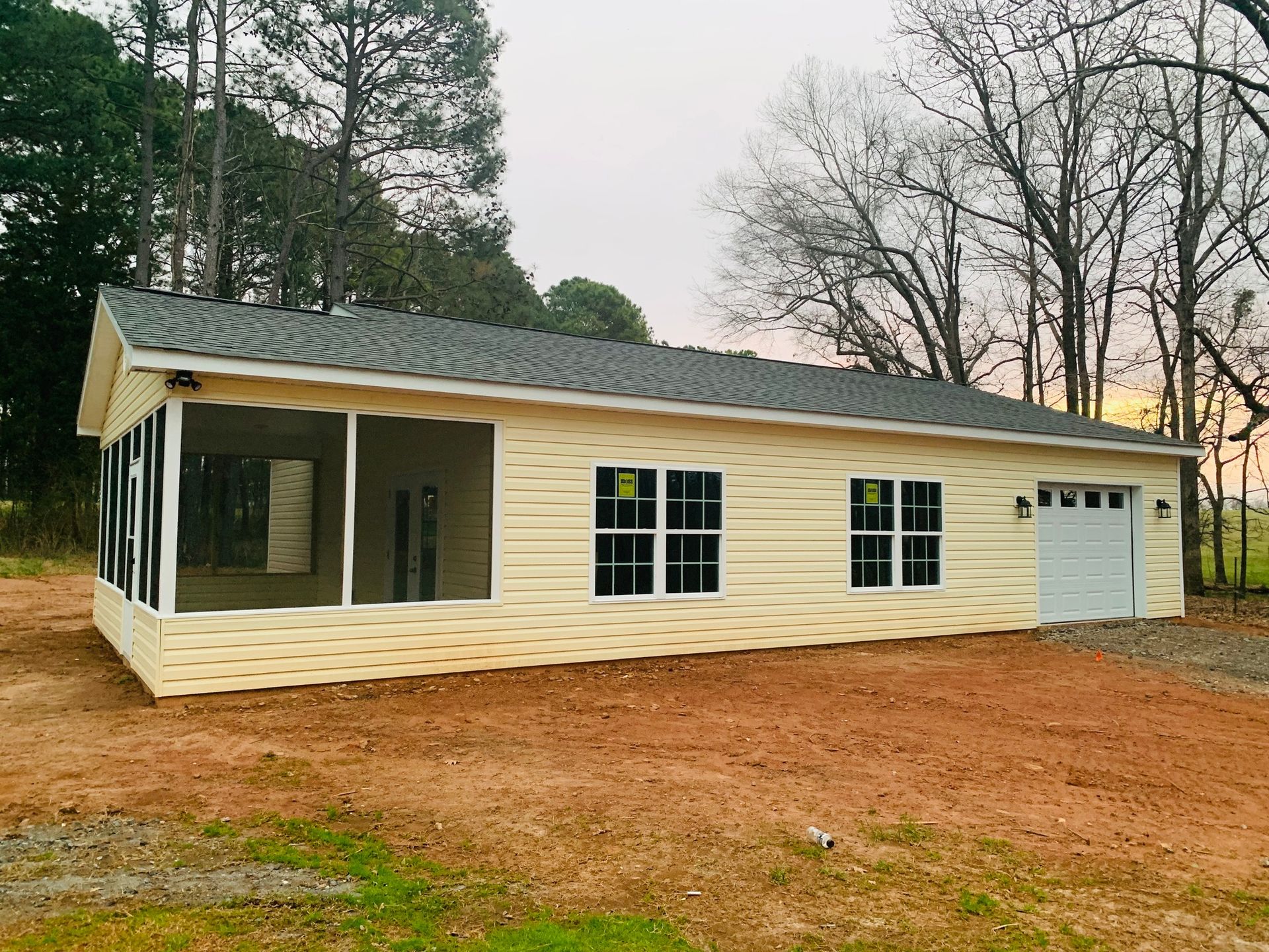Light yellow building with screened porch, windows, and garage door on a brown dirt lot.