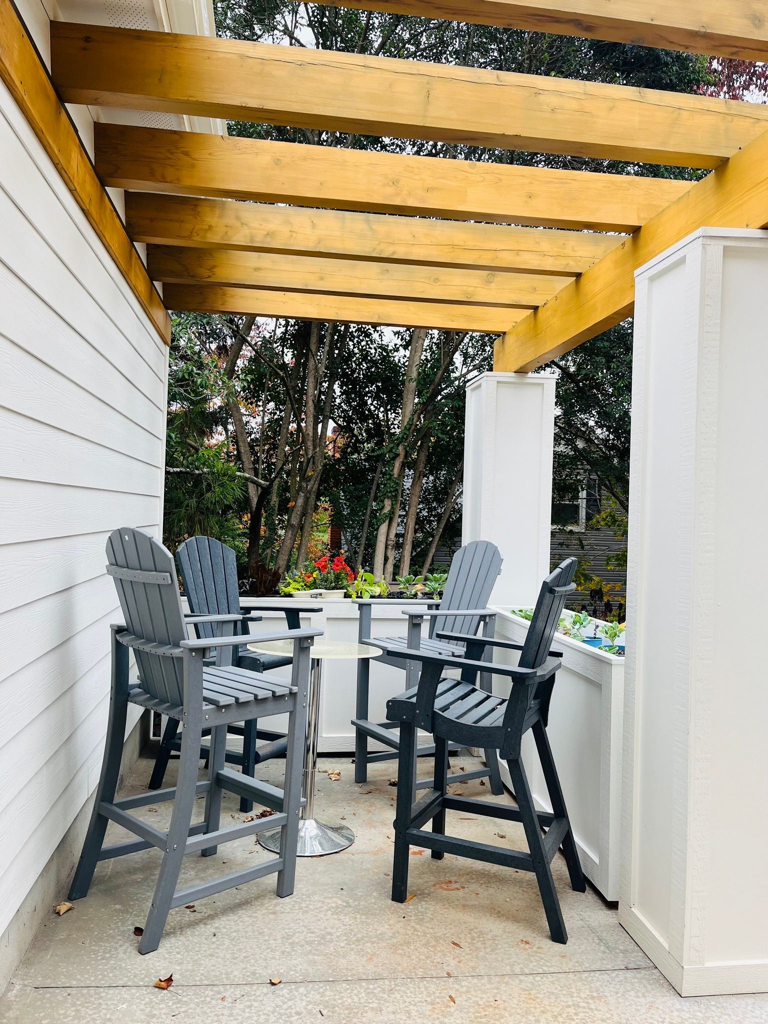 Outdoor seating area with grey chairs, white planters, and a wooden pergola roof.