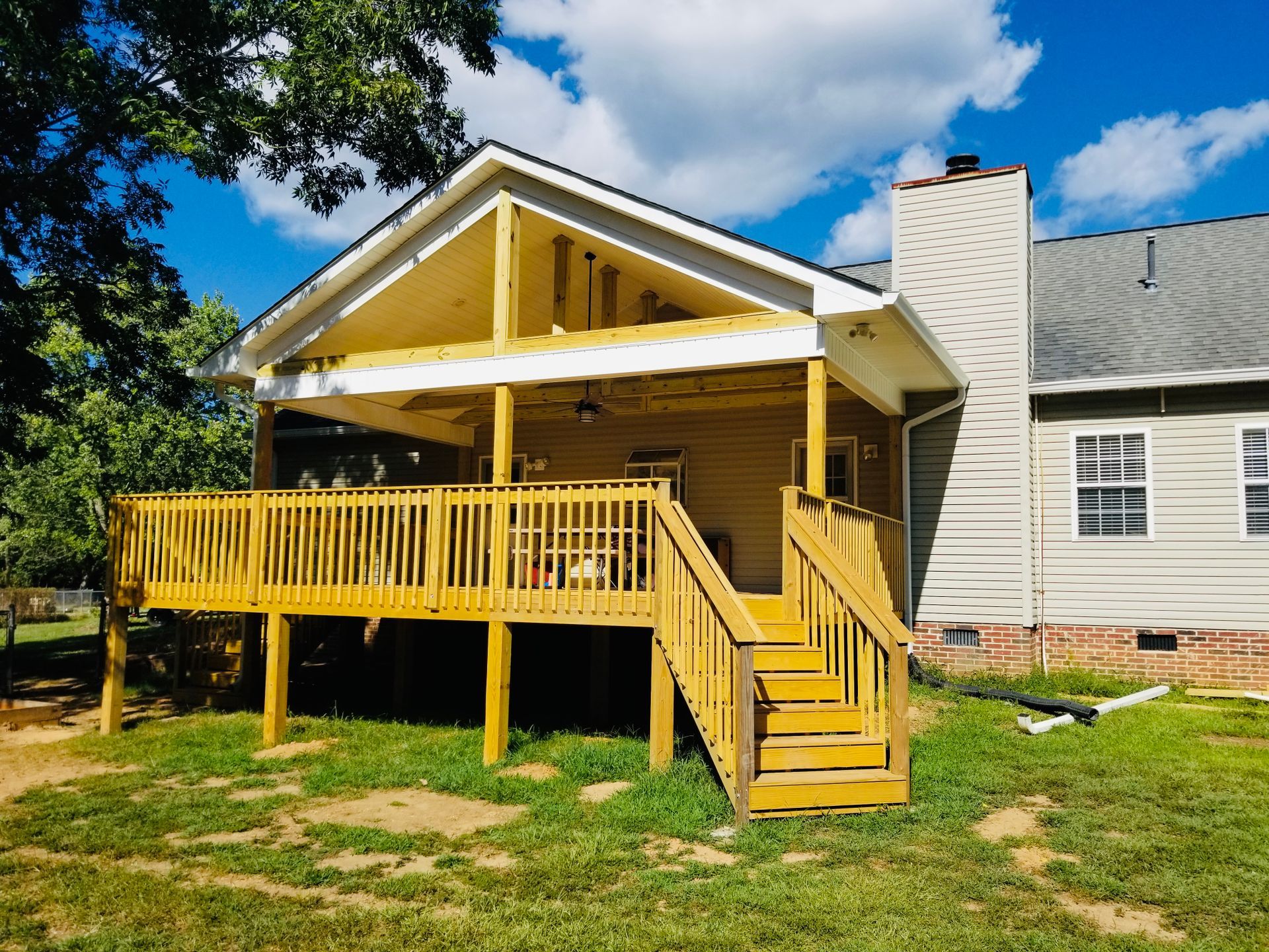 Wooden deck and covered porch attached to a house with a chimney, on a grassy yard.