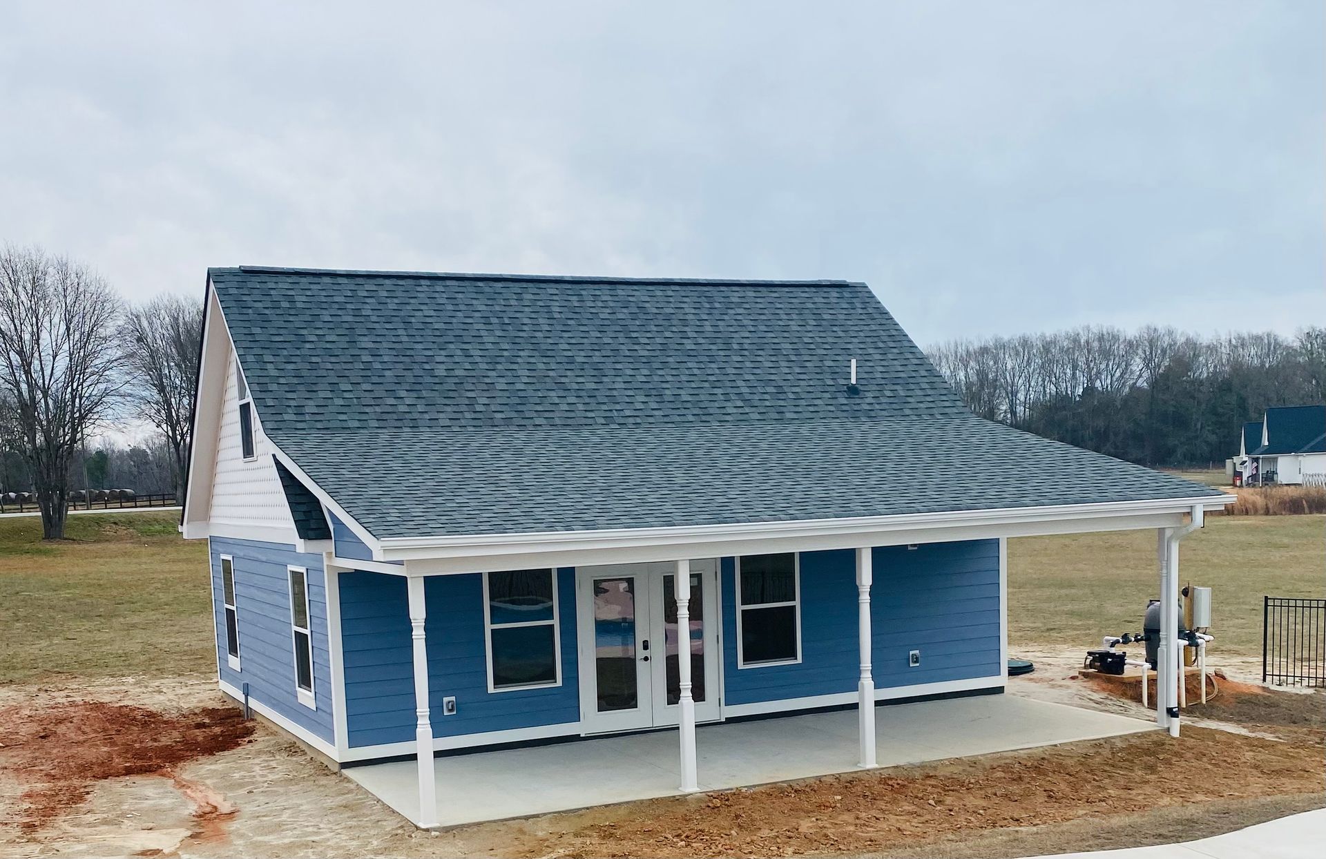 Blue house with a porch, gray roof, and white trim against a cloudy sky.