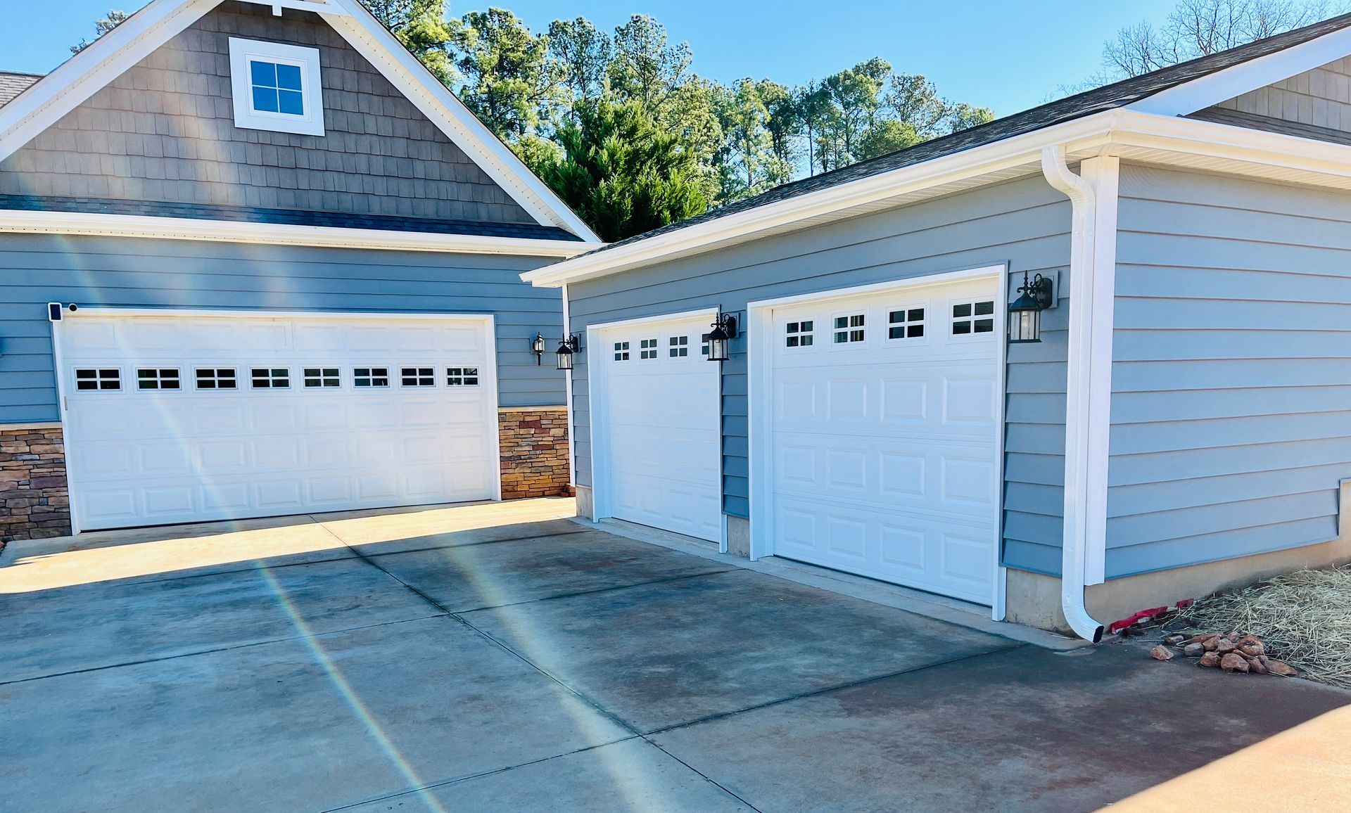 White garage doors on a light blue house, with a connecting garage.