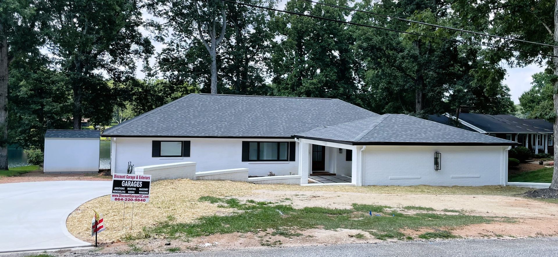 White house with a gray roof and a gravel yard. A for sale sign is in the front.