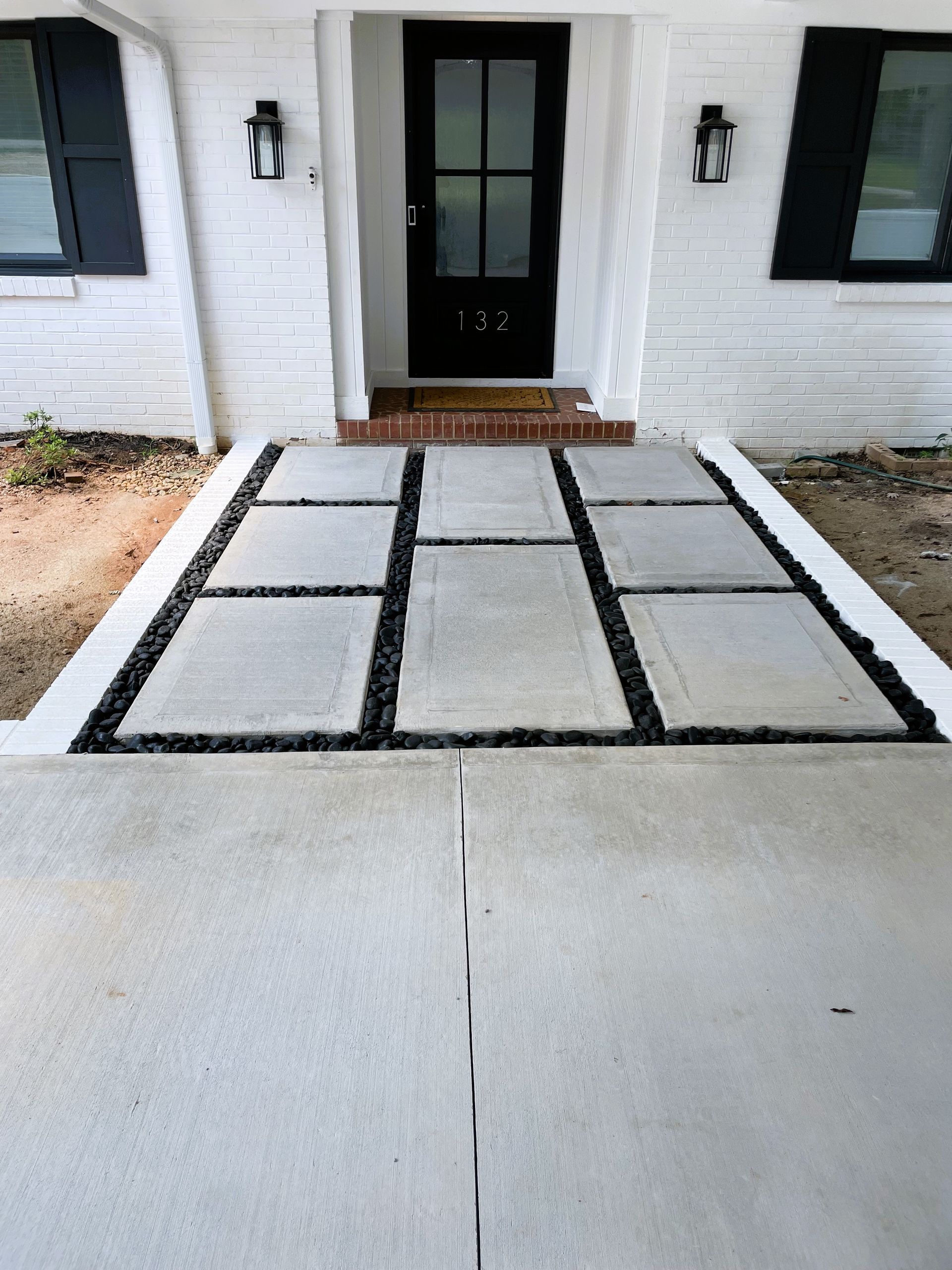 White porch with black door and walkway with stone pavers and black gravel.